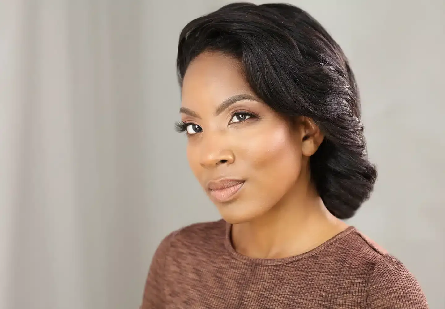 Corporate professional headshot of a woman with elegant hair and natural makeup wearing a textured brown top.