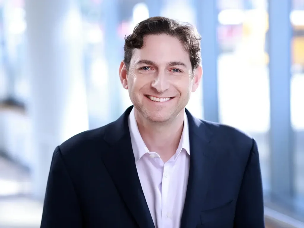 Professional Headshots: A smiling man in a dark suit against a blurred office background, modern and confident.
