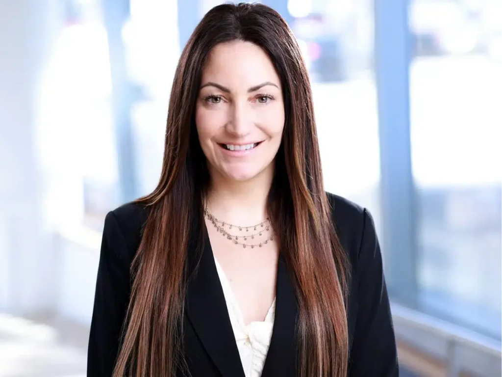 Professional corporate headshots in NYC: a smiling woman with long brown hair in a black blazer against an office background.