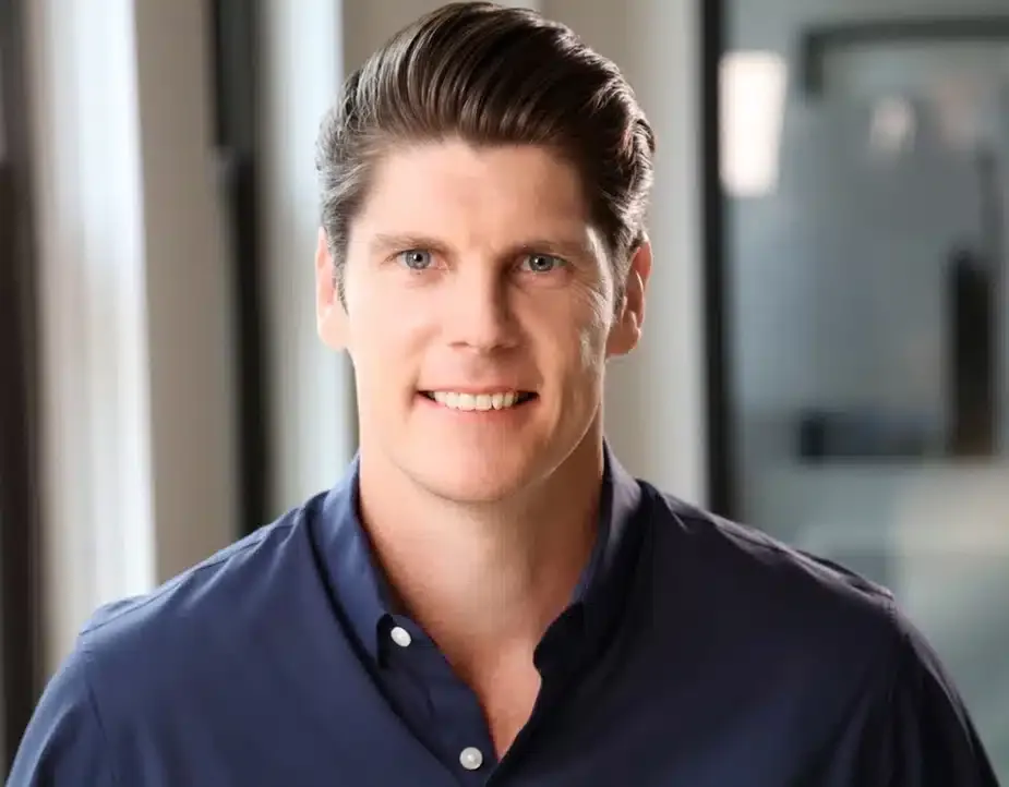 Young male professional in a navy blue shirt smiling for a modern corporate headshot in an office setting.