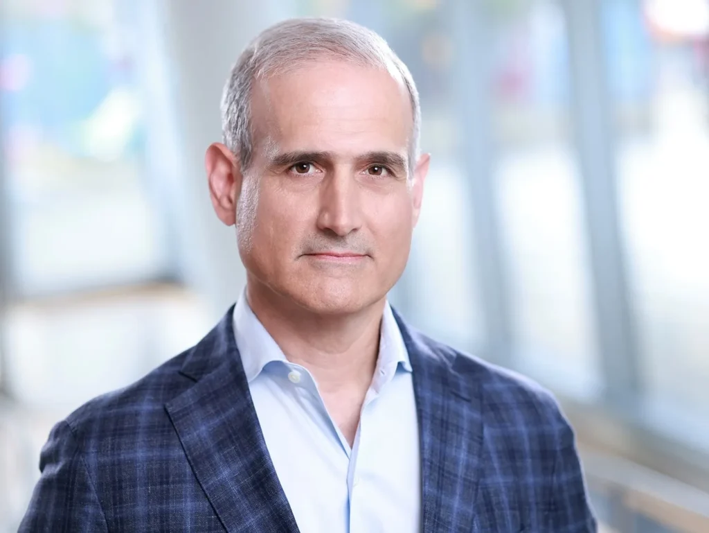 Professional man in a plaid blazer posing for corporate headshots in a bright, modern office corridor.