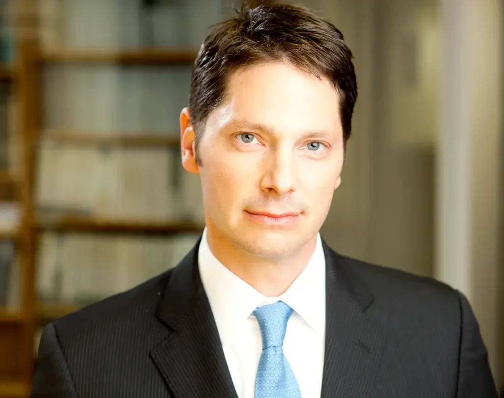 Successful businessman in a suit and blue tie posing for modern corporate headshots in a professional office environment.